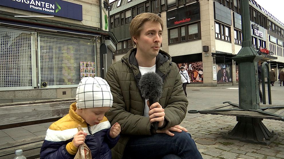 Robin sitter på en bänk i centrala Linköping bredvid sonen som leker med en pappåse.