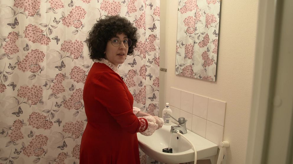 Kvinna i röd klänning tvättar händerna i badrum