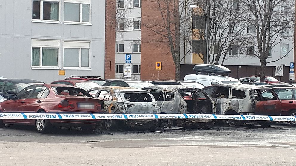 utbrända bilar på en parkering, polisens band för avspärrning i förgrunden