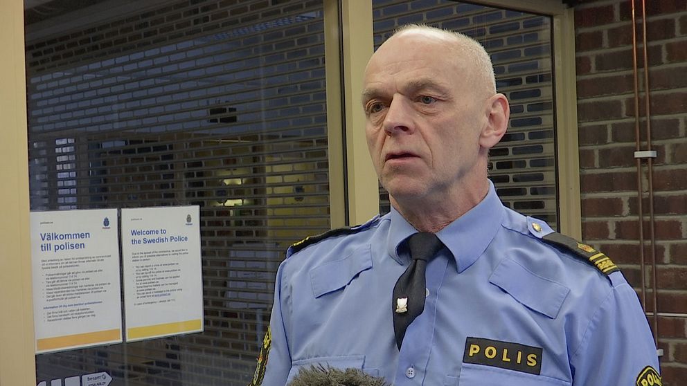 en äldre man i polisskjorta intervjuas i korridor i polishuset