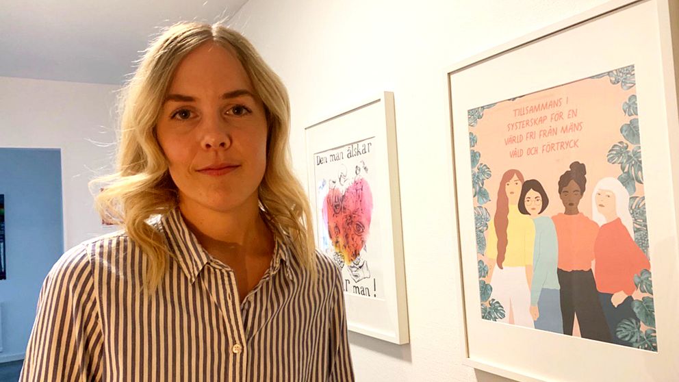 kvinna som representerar kvinnojouren i Borlänge, står framför tavlor på väggen med budskap om kamp mot våld mot kvinnor