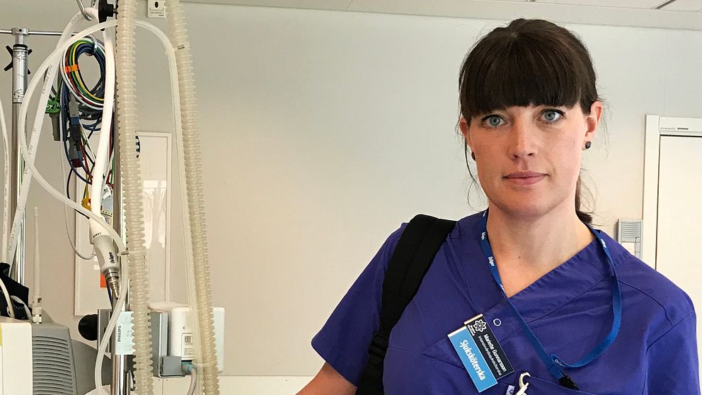 Sjuksköterskan Mariette Gunnarsson iklädd blå arbetskläder står bredvid sjukvårdsutrustning.
