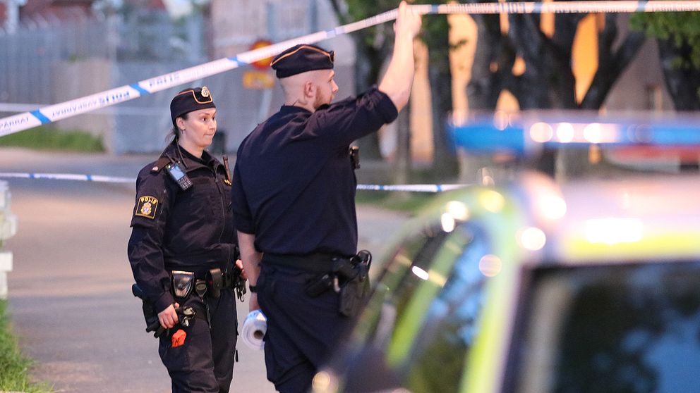 En po9liskvinna och en polisman syns framför en polisbil och är på väg in bakom avspärrningarna.