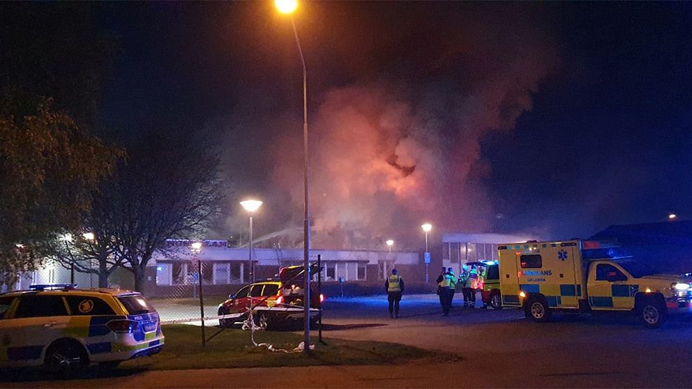 Ambulans och polisbil syns utanför en skolbyggnad. Det ryker kraftigt från byggnaden.