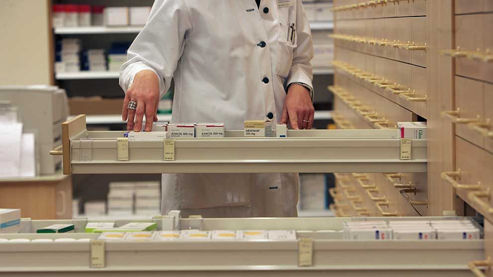 En apotekare letar efter receptbelagd medicin i en låda på ett apotek.