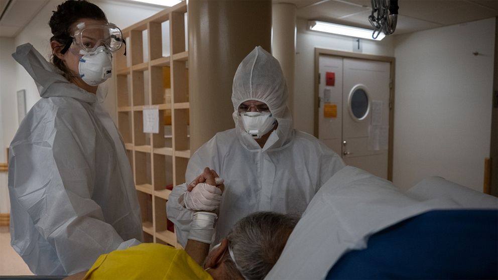 Sjukhusperson i skyddsutrustning håller en patient i handen.