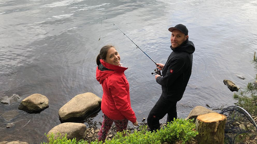 Kvinna och man står vid sjö och fiskar