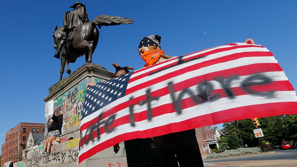 Demonstranten Andie Baker från Richmond håller upp en amerikansk flagga framför den graffititäckta statyn av sydstatsgeneralen general J.E.B. Stuart.