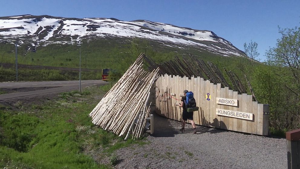 Man som går med stavar i Abisko. Bakom honom syns ett stort berg med vitt på topparna.