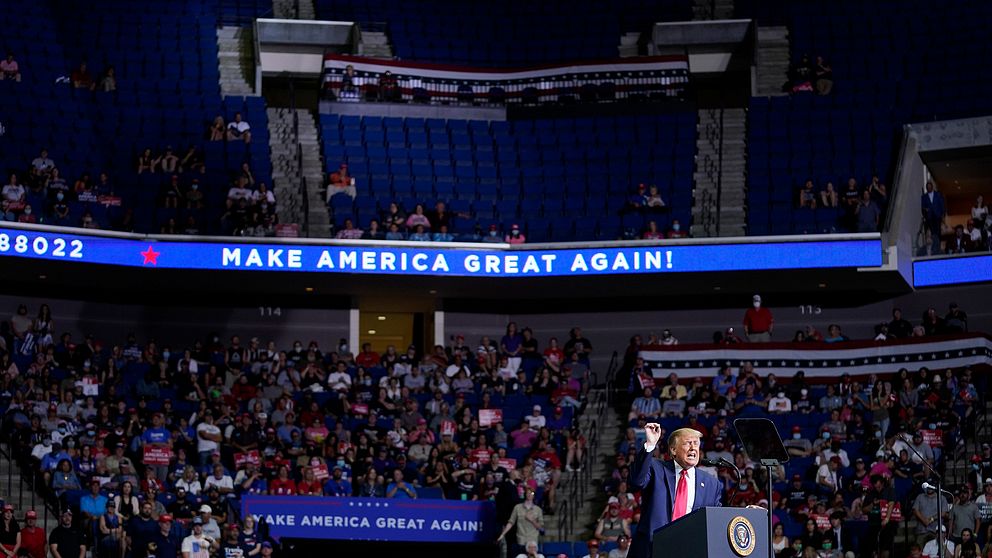 Donald Trump står vid talarstolen på scenen i en stor arena med halvtomma läktare.