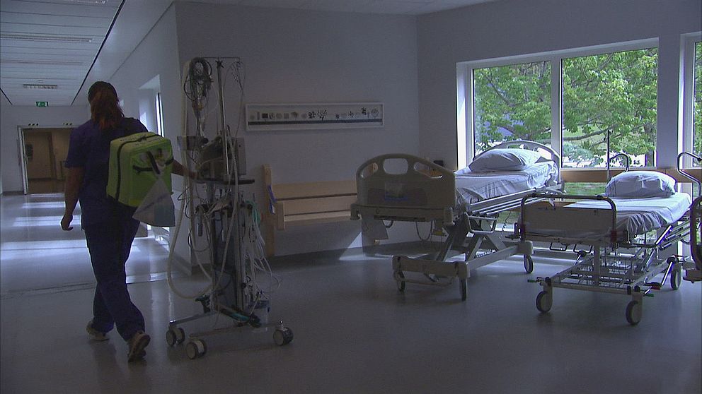 Ensam sjuksköterska går förbi två sjukhussängar.