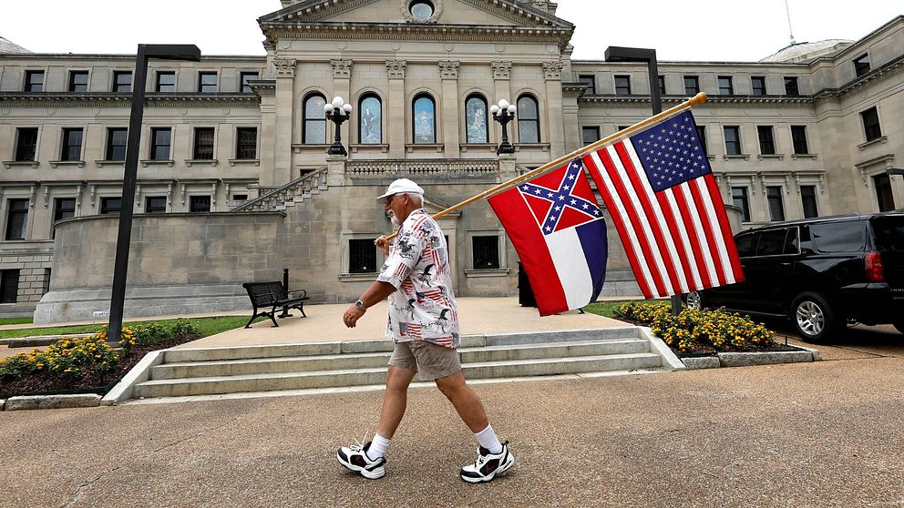 En man med den amerikanska flaggan och Mississippis nuvarande flagga med sydstatssymbolen.