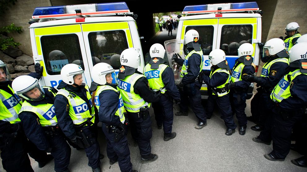 Polisstudenter övar med hjälm och skyddsväst framför två pikébussar.