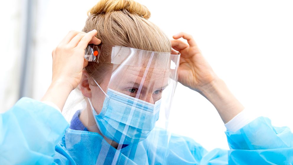 kvinna i blå sjukhusklädsel med uppsatt hår justerar skyddsvisir
