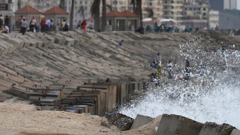 Stenpir på strand i Alexandria (arkivbild). Skummande vatten slår upp mot de stora stenarna.