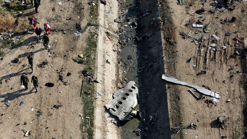 Räddningsarbetare i området där planet kraschade 8 januari i år. Man ser fragment av planbitar spridda över området.