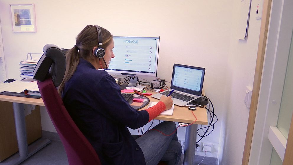 En kvinna sitter framför två datorer med ett headset och arbetar.