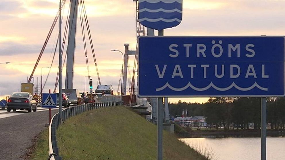 bild på en skylt med texten ”Ströms Vattudal” i förgrunden. I bakgrunden en bro med bilar.