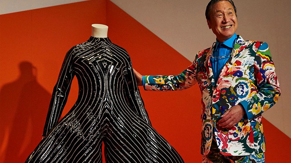 Kansai Yamamoto i färgstark mönstrad kostym vid en svartvit ballongformad dräkt han skapat åt David Bowie.