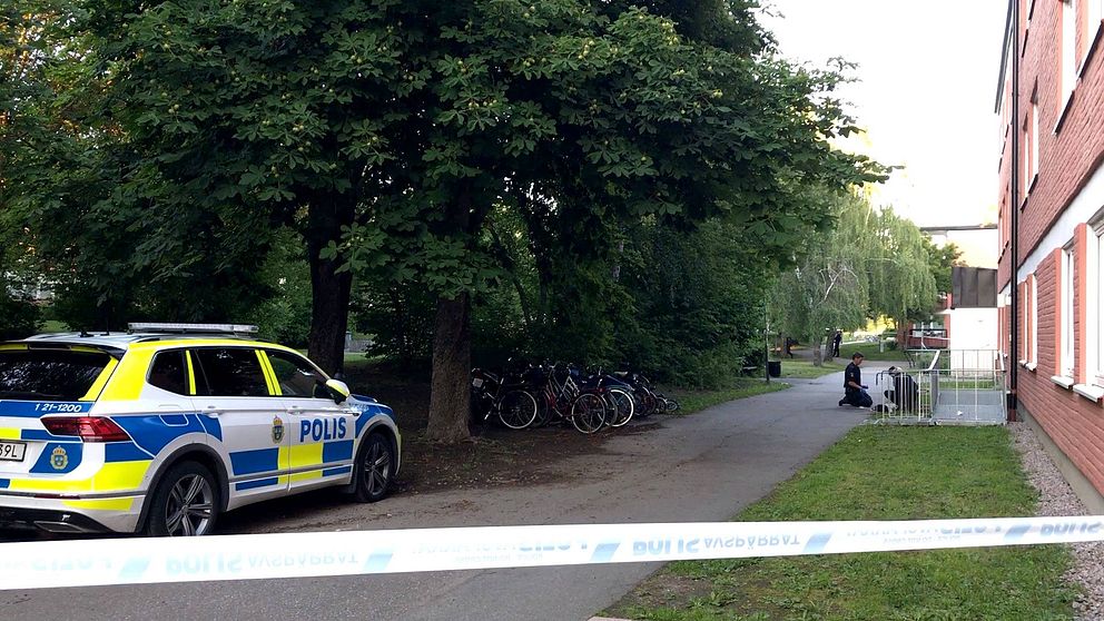 Två polisen står på knä och tittar på någonting på marken. Bredvid står en parkerad polisbil.