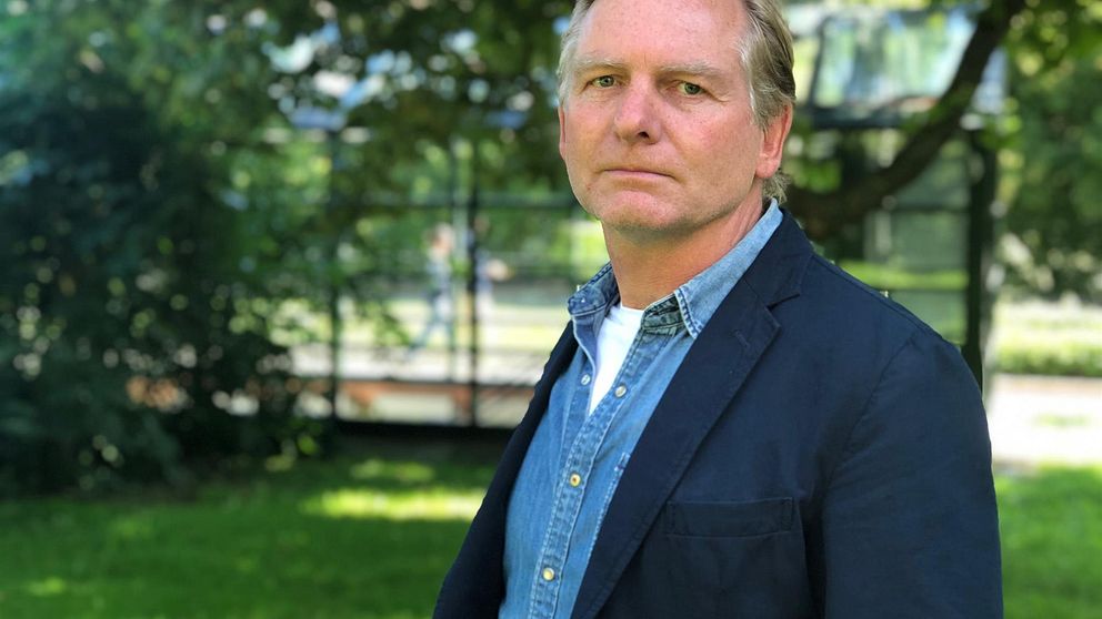 Porträttbild av polisen Fredrik Gårdare, i jeansskjorta och mörkblå kavaj. Han står i ett grönområde.