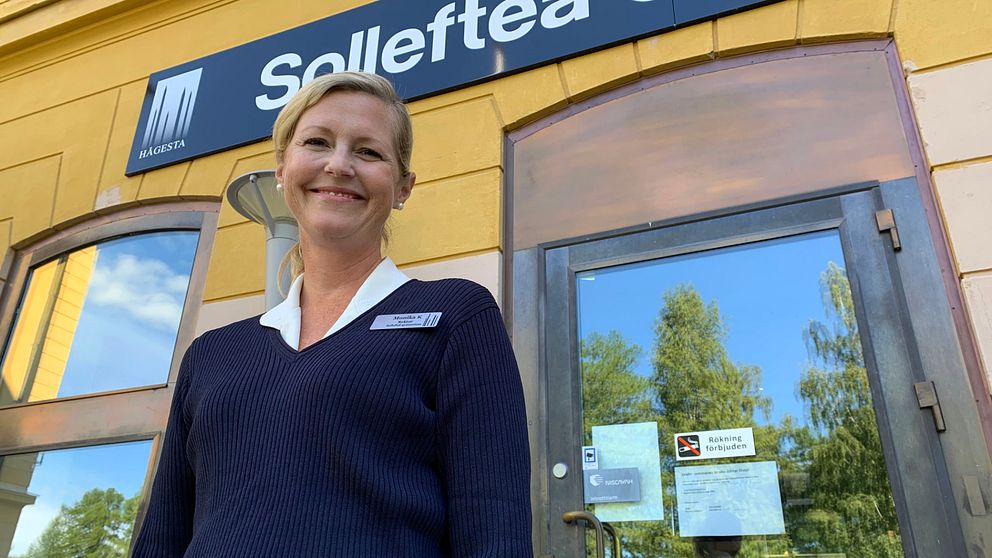 Monika Karlström, rektor vid Sollefteå gymnasium, ler mot kameran, ståendes framför skylten till Sollefteå gymnasium. Hon är iklädd en mörkblå stickad tröja och har en vit krage.