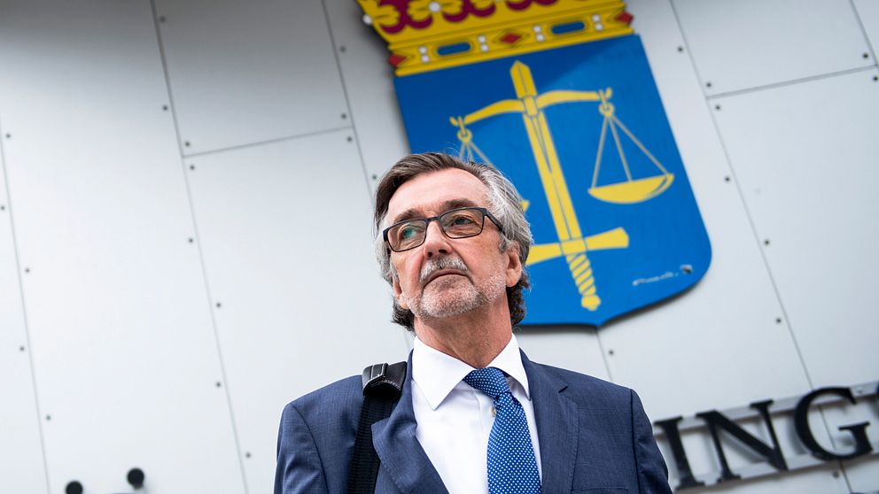 försvarsadvokat Gunnar Falk står framför domstolssymbolskylt med vågskålar