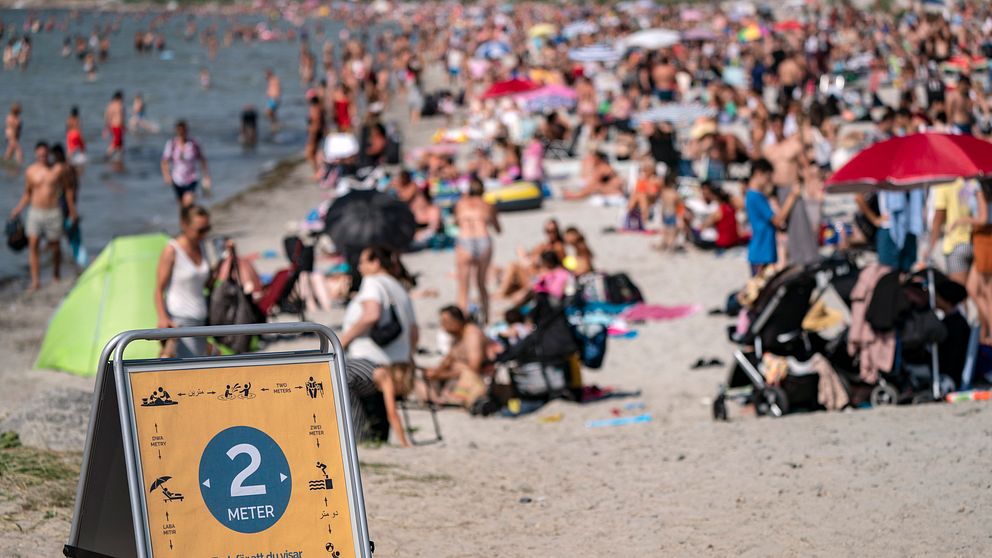 En skylt påminner om att hålla avstånd på stranden i Lomma, Skåne. Polisen i Sverige har fått in många samtal om trängsel på badstränder.