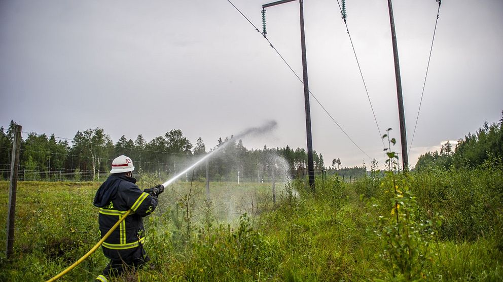 en brandman med slang sprutar vatten mot kraftledningsstolpar