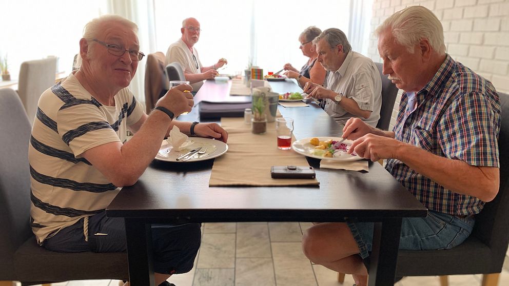 Hjalle sitter vid ett lunchbord på en restaurang tillsammans med sina vänner. Han tittar mot kameran och ler.