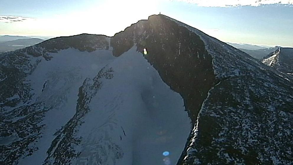 flygbild på bergstopp med brant sida med glaciär nedanför