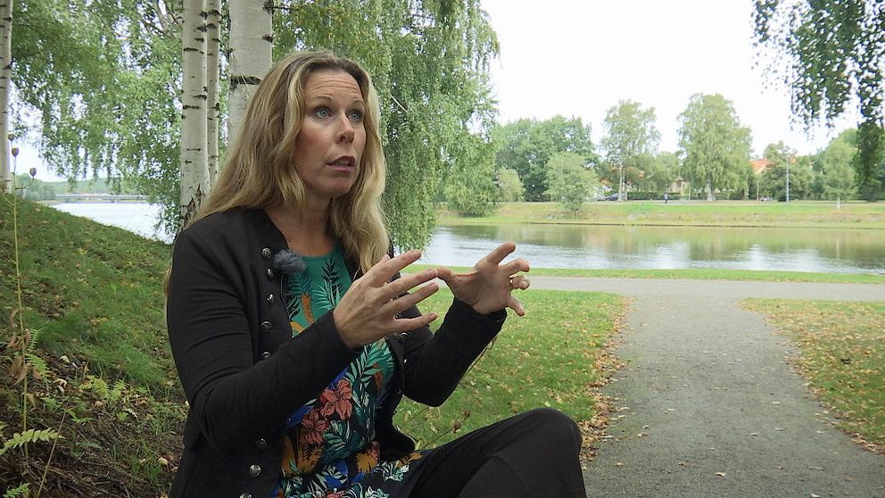 Carola Jansson sittandes i en park med Klarälven i bakgrunden.