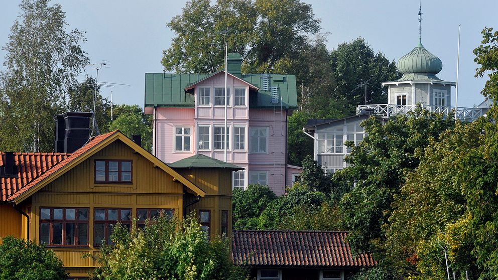 Tre kulörta villor i grönskande trädgårdar en sommardag i Vaxholm.