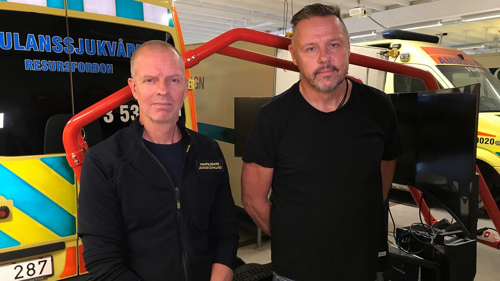 Joakim Dahlund och Jonas Åström framför simulator med skärmar och i bakgrunden riktiga ambulanser