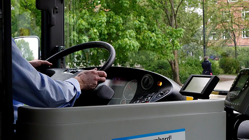 En bild på en busschaufför som kör en buss. Man ser att han håller i ratten och skog utanför fönstret.