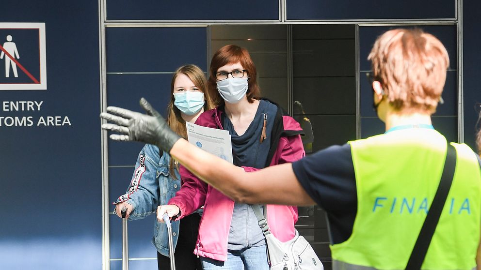 Bilden visar när resenärer anländer iklädda munskydd till Helsingfors flygplats Vantaa och guidas vidare av flygplatspersonal.