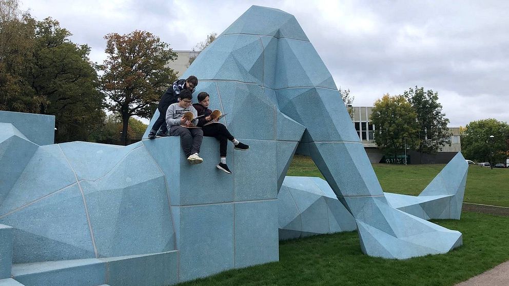 Tre pojkar sitter ovanpå en staty och läser.