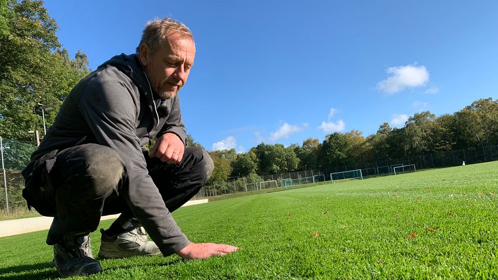 Anders Mårtensson sitter på huk och känner på gräset med sin hand