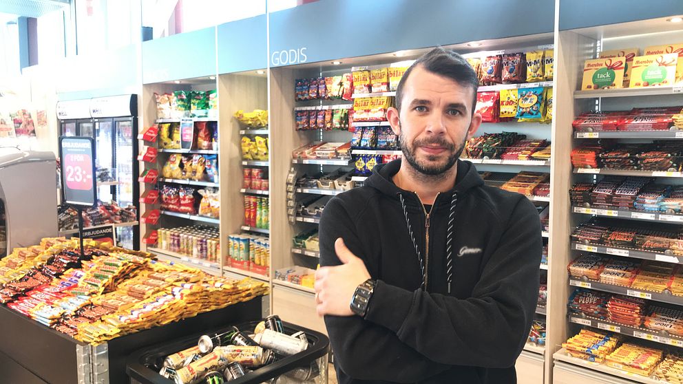 Richard Björkman står med armarna i kors i sin kiosk i stationshuset. I bakgrunden syns långa hyllor med chips, läsk och godis.