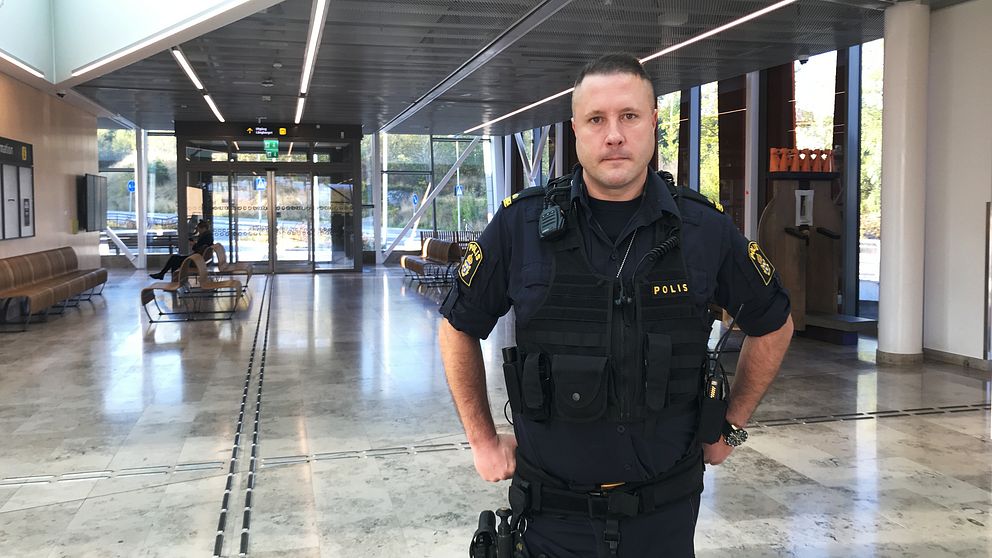 Polisen Peter Sigurd står med händerna på höften i resecentrum i Strängnäs. I bakgrunden syns informationstavlor, bänkar och glasrutor.