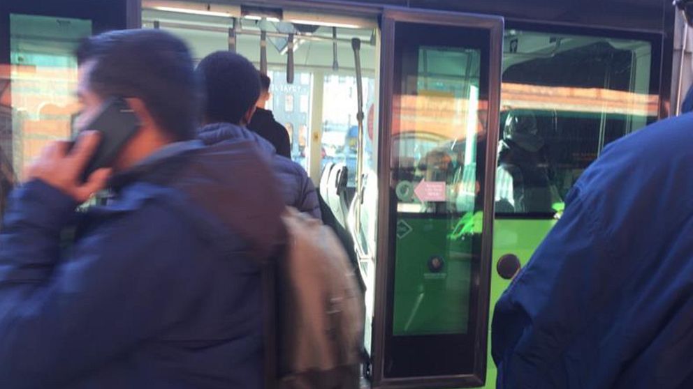 Människor vid busshållplats trängs för att komma på buss.