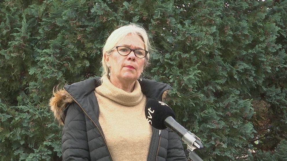 Kvinna i glasögon och tjock vinterjacka står framför en häck och pratar i en SVT-mikronfon