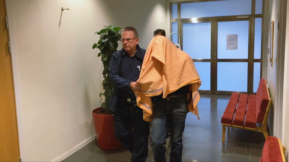 En misstänkt person förs genom en korridor med en filt över huvudet.