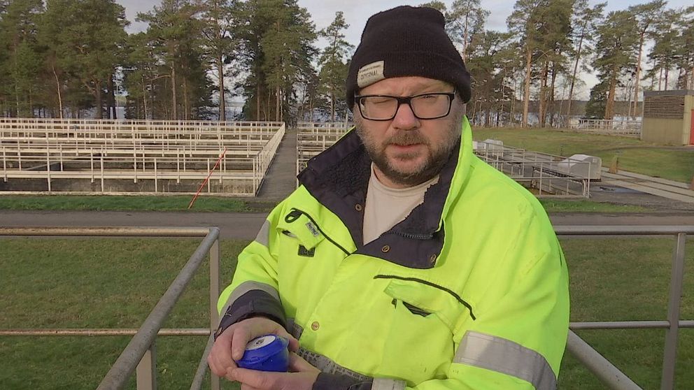 Bild på skäggig man med glasögon. Han står vid reningsverket i Östersund. Mannen är klädd i gul varseljacka och svart mössa. I händerna håller han en blå liten tratt.