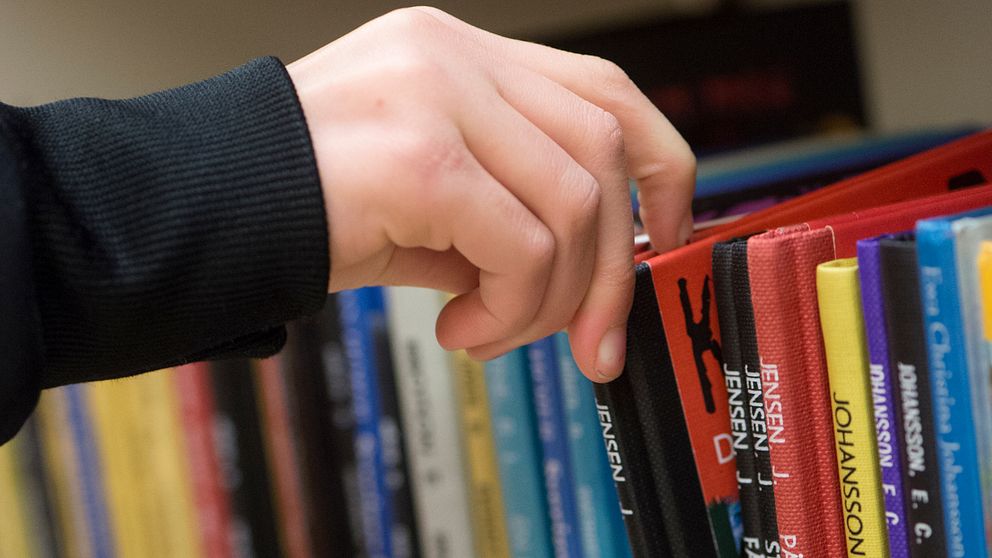 En hand plockar ut en bok från en bokhylla.