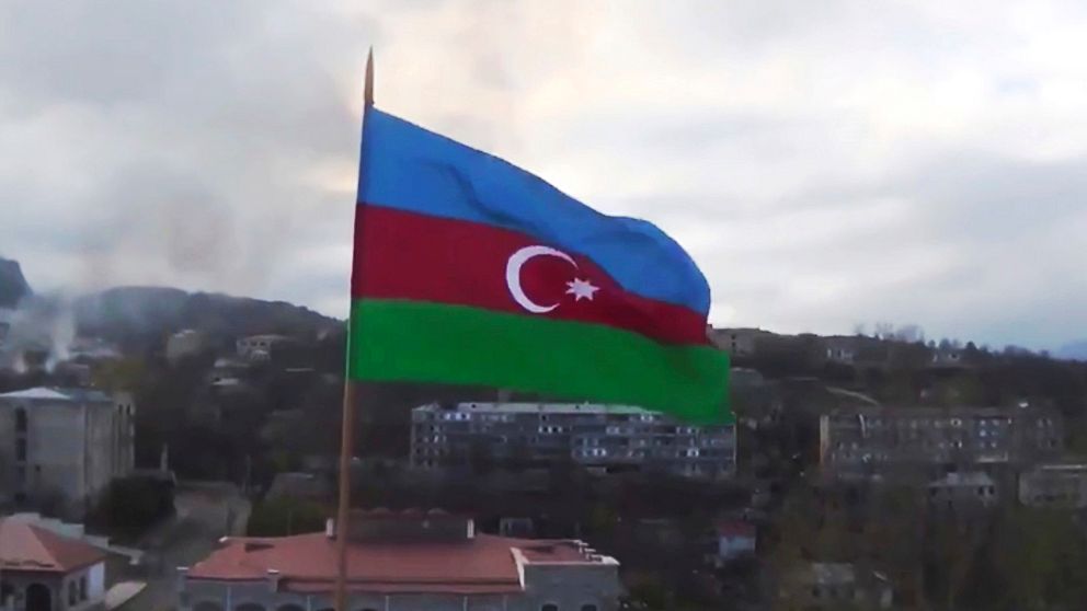 Azerbajdzjans flagga med staden Sjusji i bakgrunden, i den separatistiska regionen Nagorno-Karabakh. I bakgrunden syns även rök.