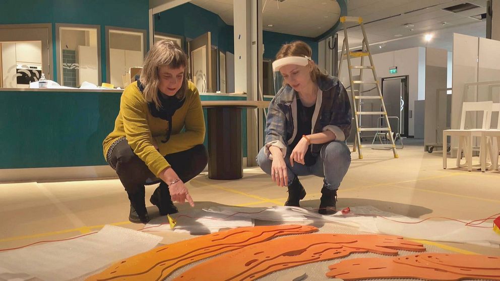Ann Skagerling och Josefine Åhs Lagerbergs sitter på huk vid ett av konstverken som ska hängas upp i Kronoteket.