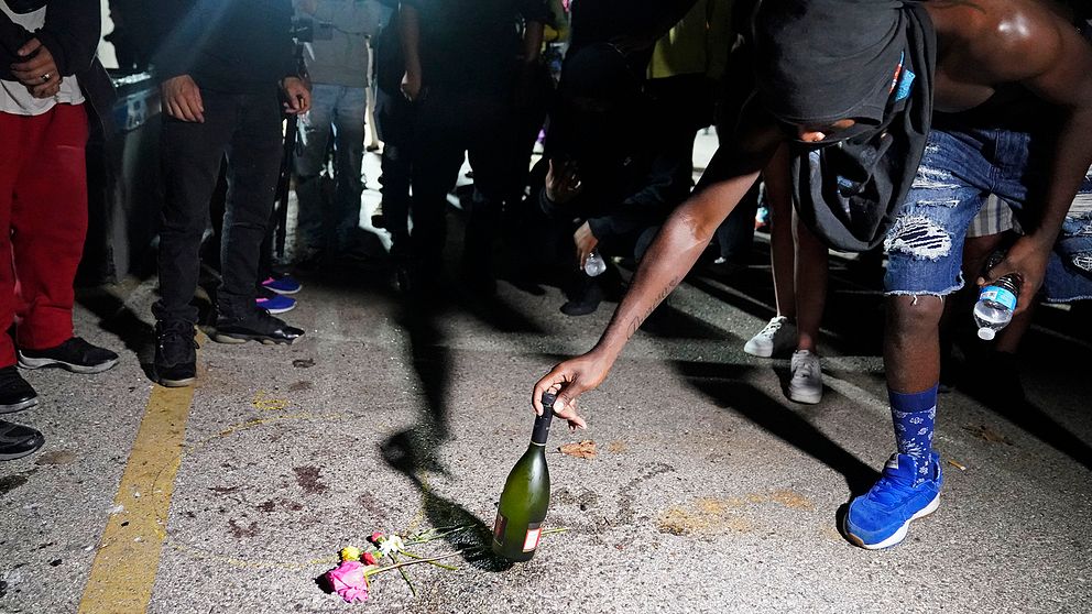 En demonstrant placerar en flaska intill ett par blommor på asfalten där en person sköts till döds under en demonstration.
