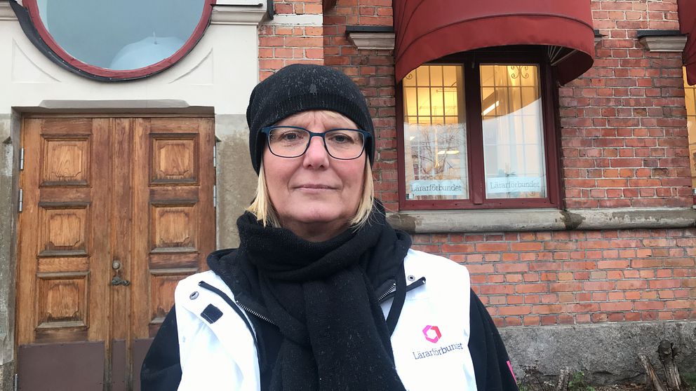 Cecilia Rahbek Nöhr står i regnet utanför Lärarförbundets lokal i Eskilstuna, den gamla busstationen i rött tegel. Hon har regn på glasögonen och en vit väst med texten ”Lärarförbundet” på.