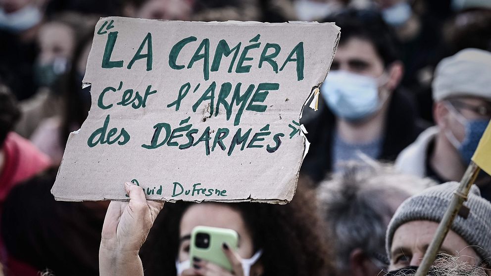 En demonstrant i Paris håller i en skylt som lyder: ”Kameran är de obeväpnades vapen”.